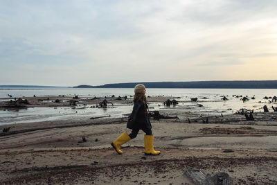 Girl in big yellow rubber boots walking at seashore