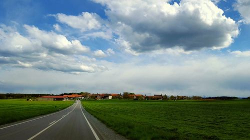 Road passing through field against cloudy sky
