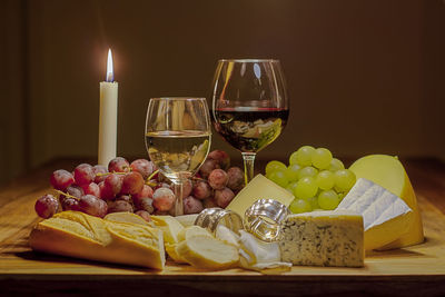 Wineglasses with cheese and fruits on table by illuminated candle