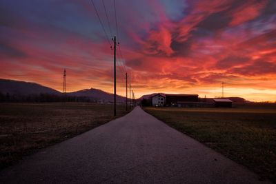 Road amidst field against sky during sunset