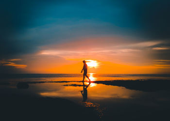 Silhouette person standing on beach against sky during sunset
