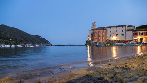 Illuminated buildings by sea against clear blue sky