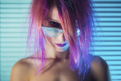 Close-up portrait of topless young woman with purple hair wearing sunglasses against wall