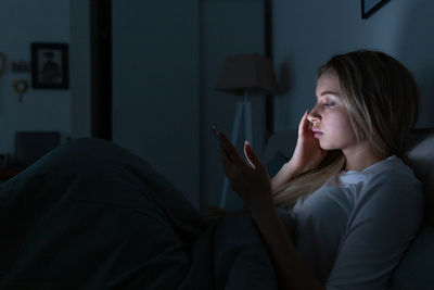 Side view of woman using mobile phone on bed at home