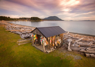 Hut by sea against cloudy sky during sunset