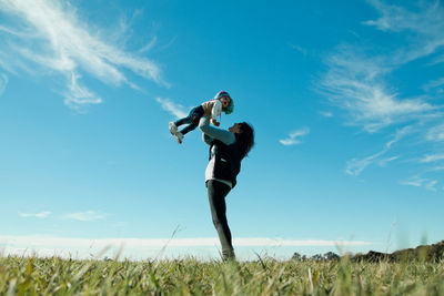 Low angle view of grandmother carrying granddaughter while standing on land against blue sky