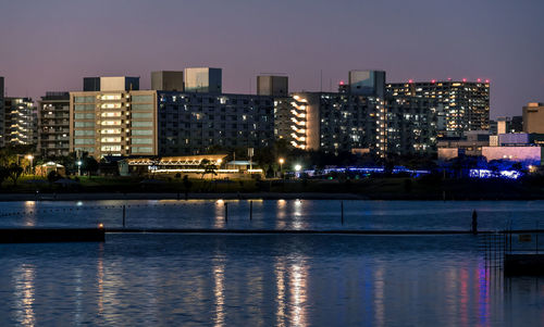 Illuminated buildings by river against sky in city at night