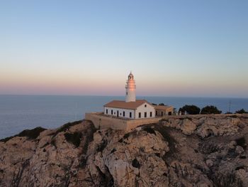 Lighthouse by sea against clear sky