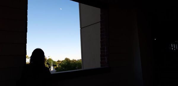 Silhouette man standing by window against clear sky