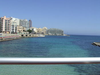 Sea by buildings against clear blue sky