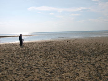 Mother walking with her baby at beach against sky