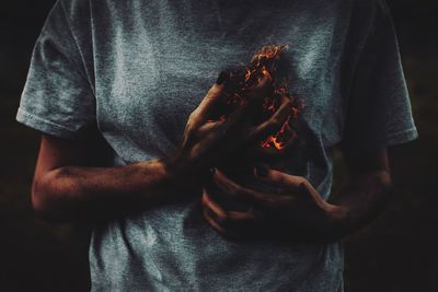 Digital composite image of woman in gray t shirt holding fire against black background