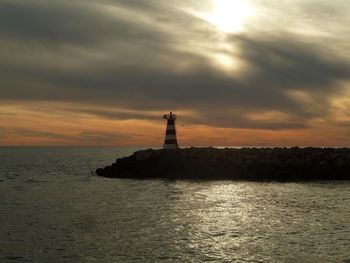 Lighthouse by sea against cloudy sky