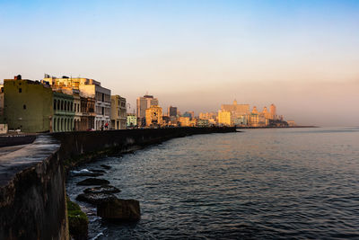 Sea by buildings against sky at sunset