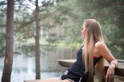 Young woman sitting on picnic table by lake