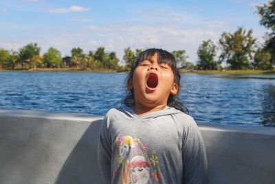 Cute girl yawning against lake 