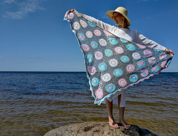 Woman standing on rock by sea against sky