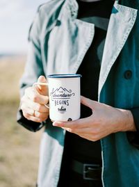 Midsection of man having coffee while standing on field