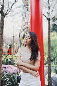 Young woman looking down while standing against plants in park