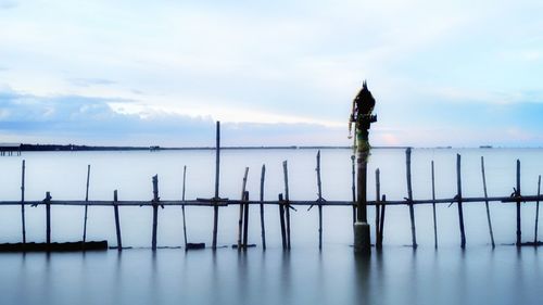 Silhouette wooden posts in sea against sky