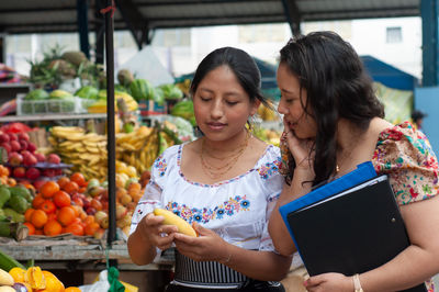 Portrait of smiling friends using mobile phone while sitting at market