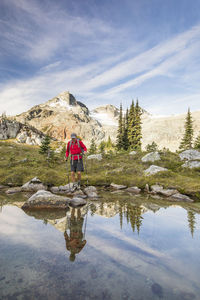 Reflection of backpacker balancing on rocks next to alpine lake.