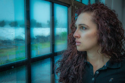 Portrait of young woman looking through window