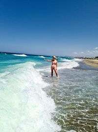 Rear view of woman standing at beach against clear blue sky