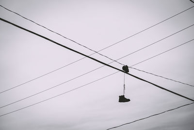 Low angle view of shoes hanging on cable against sky