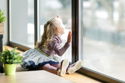 Girl looking through window while sitting at home