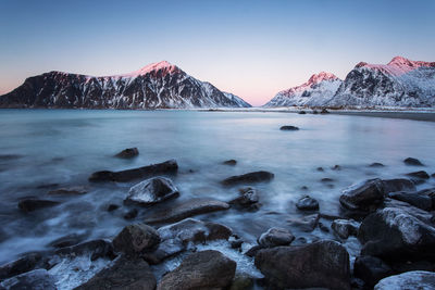 Scenic view of sea by snowcapped mountains against sky during winter