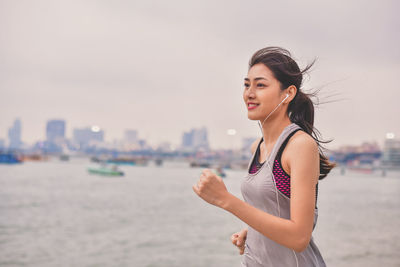 Woman listening music while jogging by river against sky