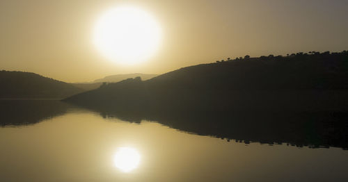 Scenic view of river with silhouette mountains reflection at sunset