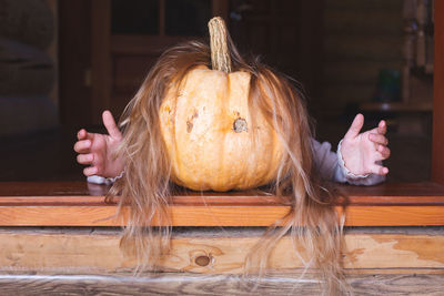 On a threshold lies a orange pumpkin with hair and arms, stretching out his arms forward. halloween