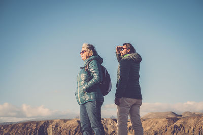 People looking away while standing against blue sky