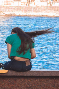 Rear view of woman sitting on ledge at riverside