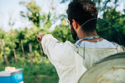 Rear view of beekeeper pointing on land