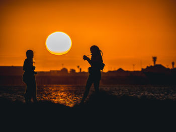 Silhouette people photographing at lakeshore during sunset