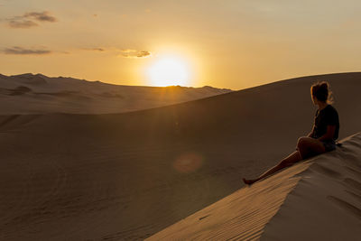 Woman sitting on land against sky during sunset