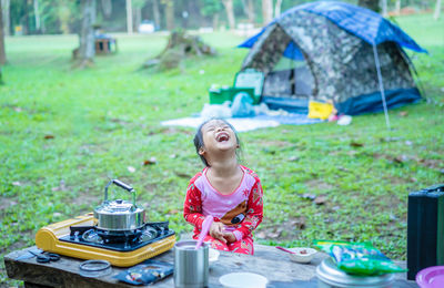 Girl laughing while sitting at table during camping in forest