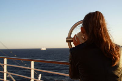 Woman looking through binoculars by railing against sky