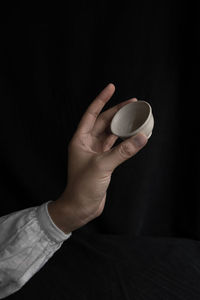 Cropped hand holding empty bowl against black background