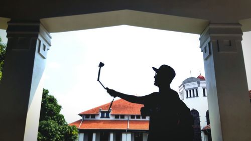 Low angle view of silhouette man taking selfie against buildings