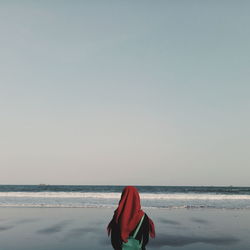 Rear view of woman in hijab standing at beach against clear sky