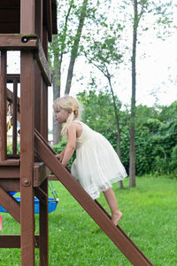 Side view of girl standing on ladder in playground against trees
