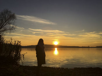 Silhouette woman standing by lake against sky during sunset