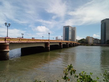 Bridge over river by buildings against sky