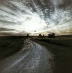 Road passing through field against cloudy sky