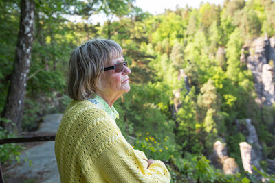 Side view of senior woman wearing sunglasses standing in forest