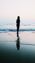 Silhouette woman standing on beach against clear sky